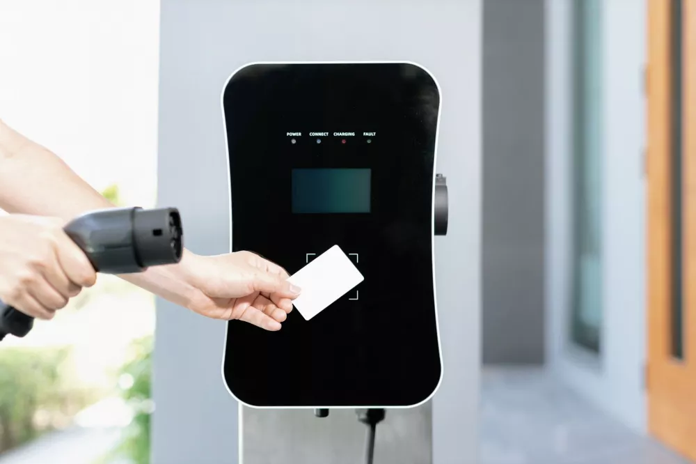 Kierowca przyklada karte platnicza do czytnika ladowarki samochodu elektrycznego