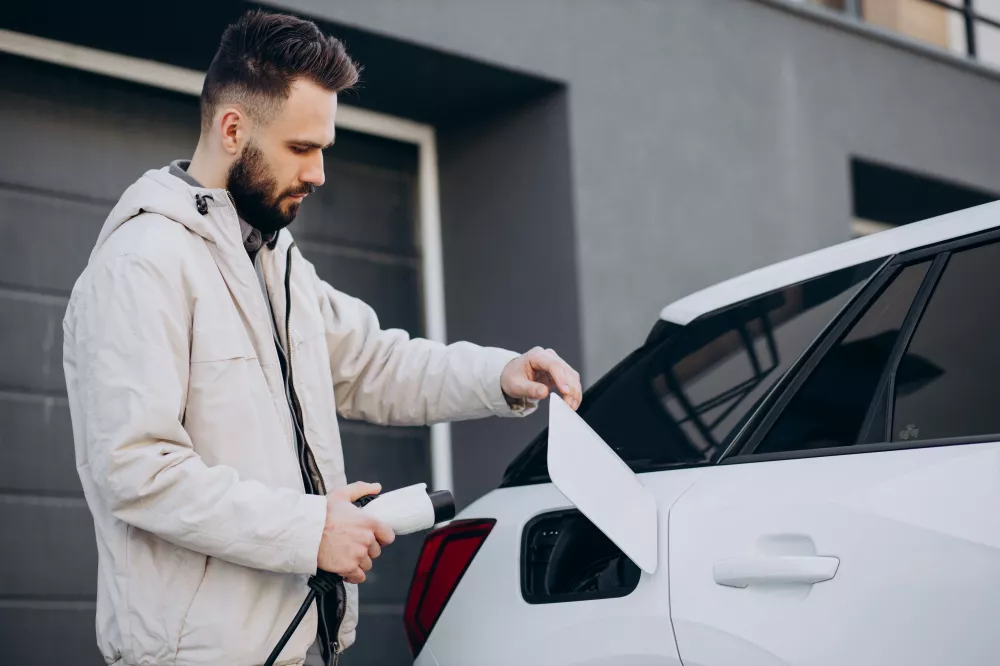 man-charging-electric-car-by-house